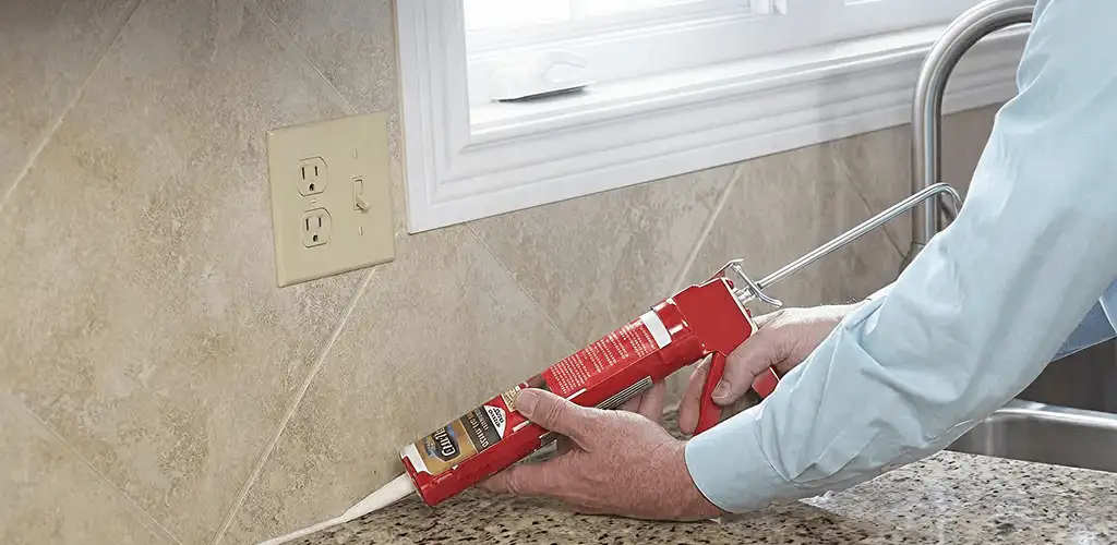 Handyman applying caulk along a kitchen backsplash and countertop seam in Orlando, FL